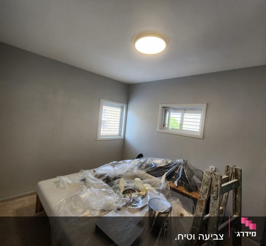 סולם וחפצים מכוסים בניילון בחדר צבוע אפור